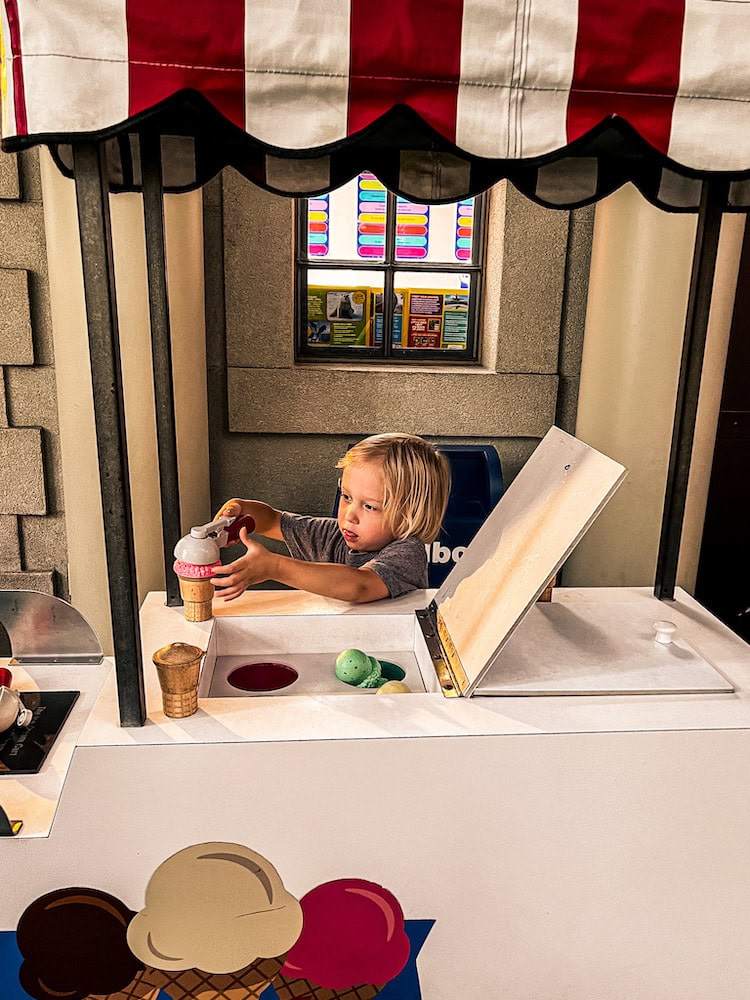 Child pretending to serve ice cream at a play ice cream cart inside The Magic House children’s museum in St. Louis.