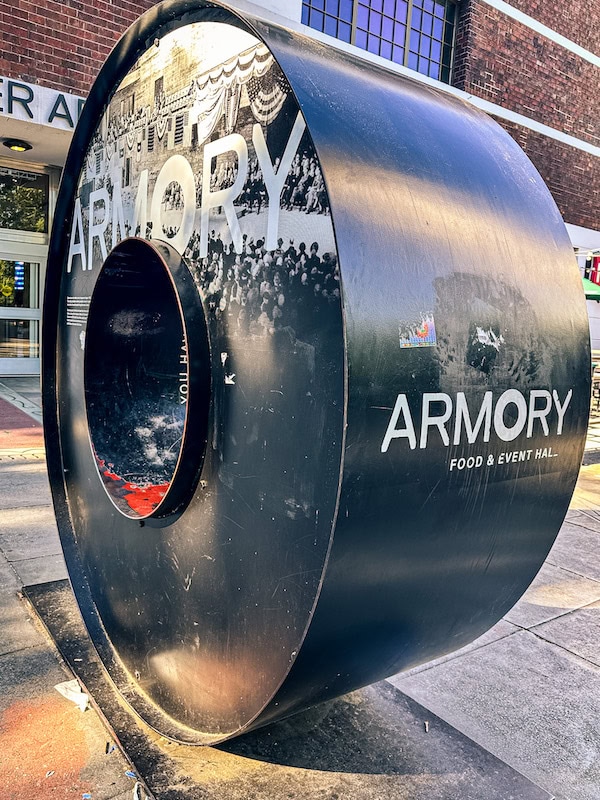 Large circular black sculpture labeled “Armory Food & Event Hall” outside the Seattle Center Armory building.