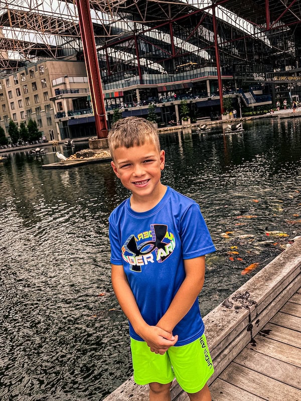 Child standing beside the koi pond at Union Station in St. Louis, with the covered train shed and buildings in the background.