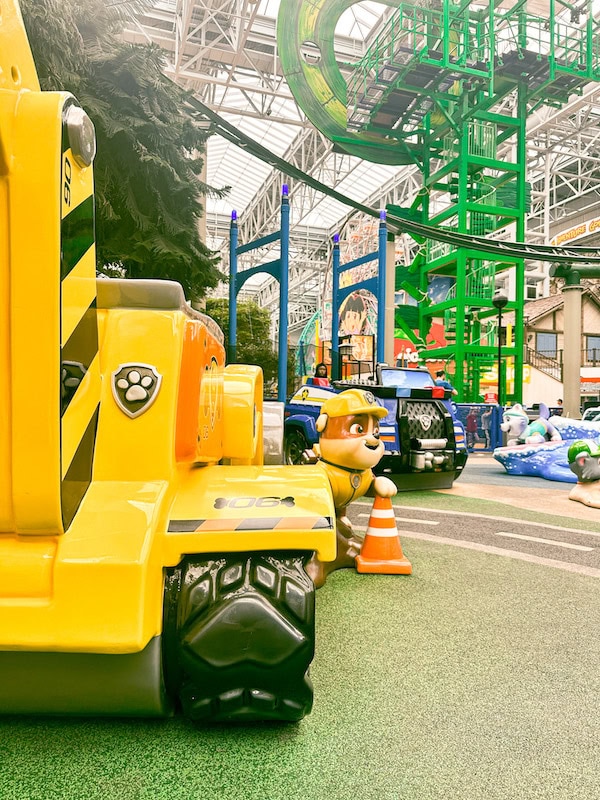 Paw Patrol’s Rubble and his yellow construction truck at the Adventure Bay play area inside Nickelodeon Universe at the Mall of America, with colorful rides and attractions in the background.