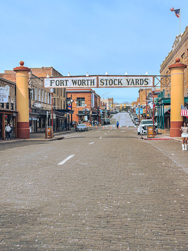 Wide view of Exchange Avenue under the Fort Worth Stockyards sign with historic buildings and cobblestone street