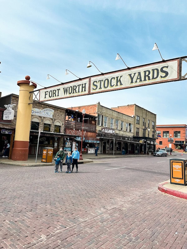 Kids standing under the Fort Worth Stockyards sign on Exchange Avenue with historic buildings in the background
