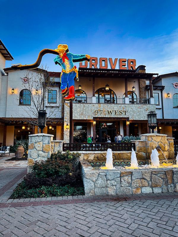 Hotel Drover exterior with neon cowboy sign, fountain, and 97 West Kitchen entrance in Mule Alley at the Fort Worth Stockyards