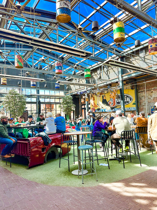 Bright open-air indoor dining space at Second Rodeo Brewing with large windows, hanging decor, and families eating in Mule Alley at the Fort Worth Stockyards