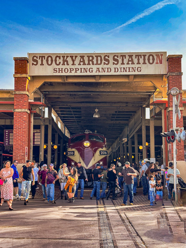 Crowds walking through Stockyards Station shopping and dining area with a vintage train inside at the Fort Worth Stockyards