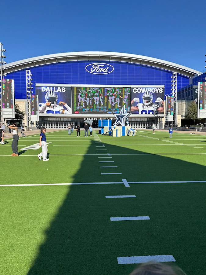 Kids running on the turf at Tostitos Championship Plaza outside Ford Center at The Star in Frisco, Texas, with large Dallas Cowboys screen in the background