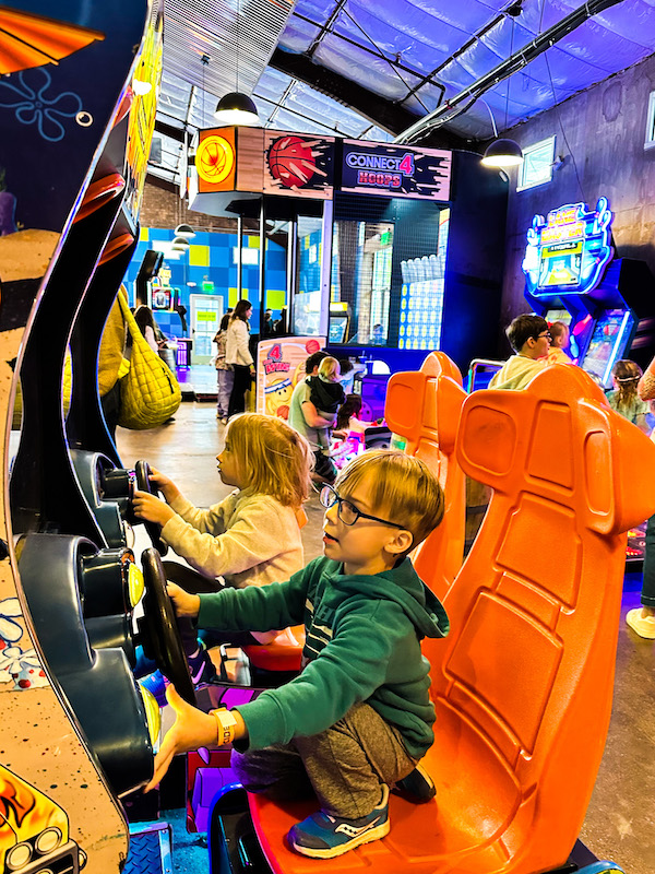 Kids playing arcade racing games at Cidercade in Fort Worth, Texas with colorful machines and interactive games in the background
