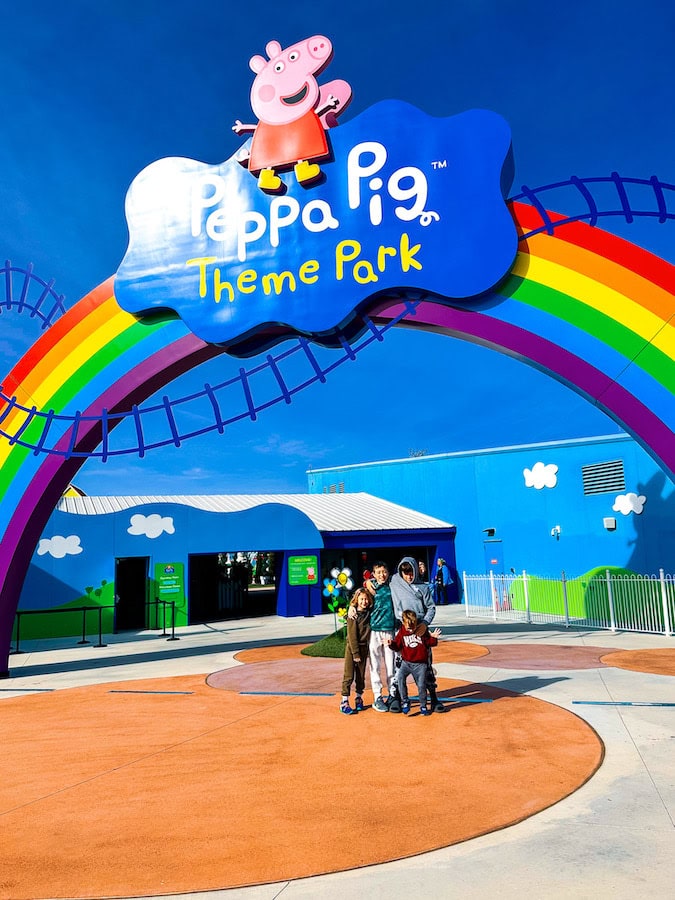 Kids standing under the Peppa Pig Theme Park entrance sign with rainbow arch in North Richland Hills, Texas