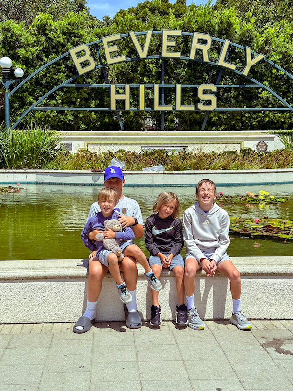Four boys sitting in front of the Beverly Hills sign and lily pond in Beverly Hills, California.