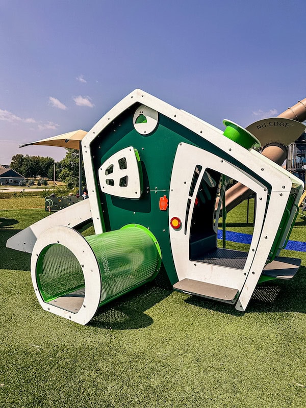 Green and white toddler playhouse with a crawl tunnel at Centennial Park in Waukee, Iowa.