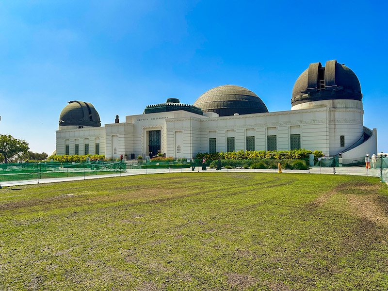 Griffith Observatory in Los Angeles with its iconic domes, lawn, and clear blue sky.