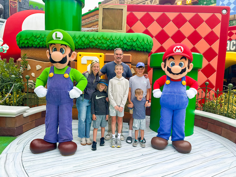 Family of six posing with Mario and Luigi characters inside Super Nintendo World at Universal Studios Hollywood during an early morning visit.