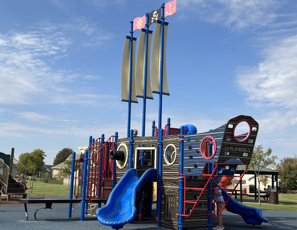 Pirate ship-themed playground with blue slides, climbing features, and tall sails at Ironwood Park in Altoona, Iowa.