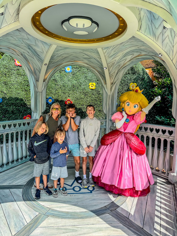 Family posing with Princess Peach inside Super Nintendo World at Universal Studios Hollywood.