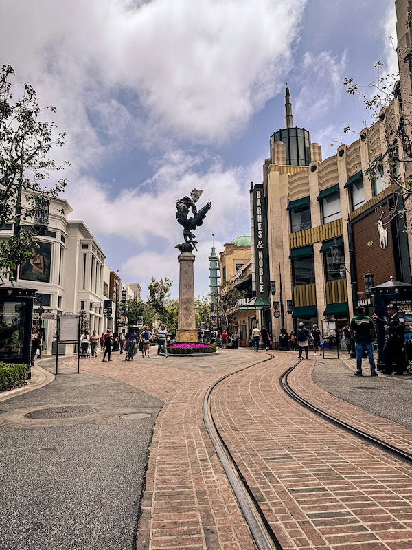 Main shopping promenade at The Grove in Los Angeles with trolley tracks, storefronts, and the Barnes & Noble sign visible in the background.