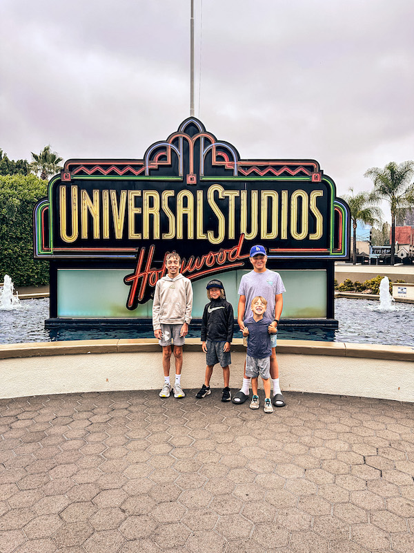 Three boys posing in front of the Universal Studios Hollywood entrance sign before a day at the theme park.