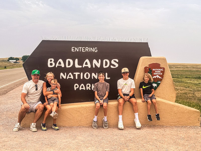 Family of six posing in front of the Badlands National Park entrance sign in South Dakota.