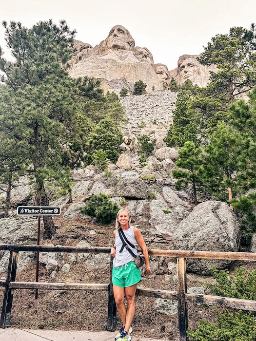 Woman standing along the Presidential Trail with Mount Rushmore National Memorial rising above the trees in South Dakota.