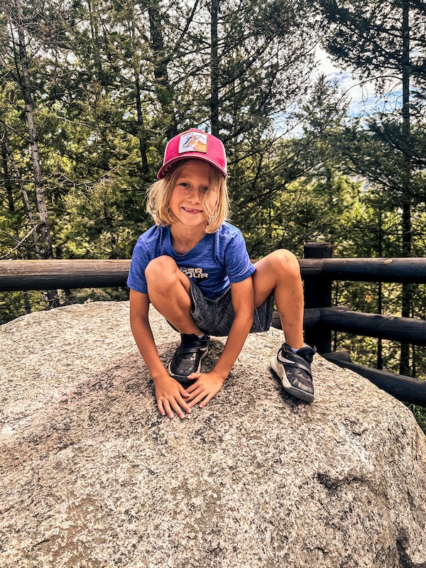 Boy climbing on a large boulder near Tower Fall Overlook in Yellowstone National Park.
