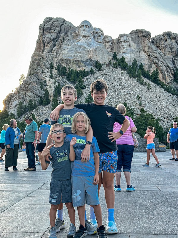Four children posing in front of Mount Rushmore National Memorial during a family vacation in South Dakota.