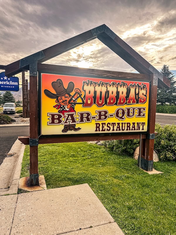 Colorful Bubba’s Bar-B-Que Restaurant sign along the road in Cody, Wyoming, with mountains visible in the distance.