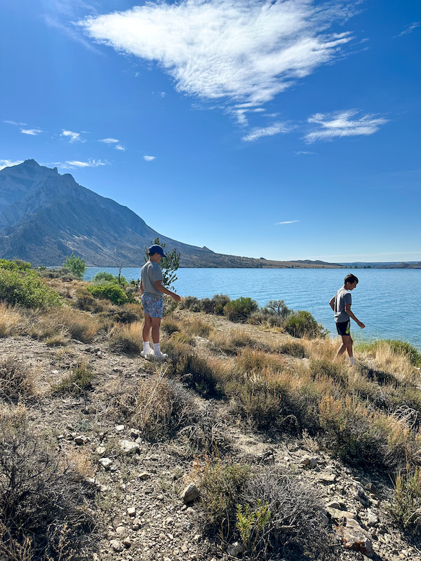 Two boys exploring the rocky shoreline of Buffalo Bill Reservoir with mountain views in Buffalo Bill State Park, Wyoming.