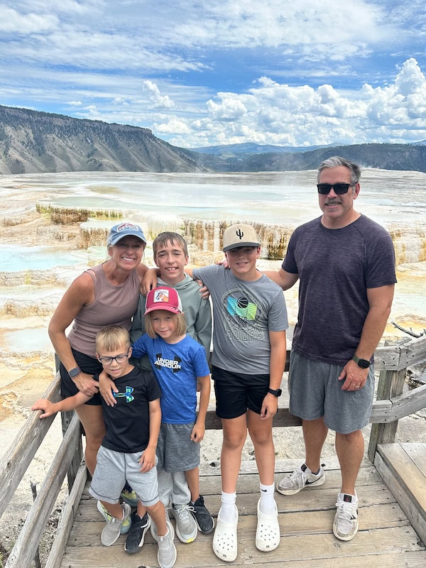 Family of six standing on the boardwalk with the colorful terraces and mountain views at Mammoth Hot Springs in Yellowstone National Park.