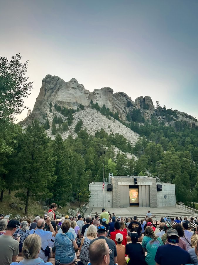 Crowd seated at the Mount Rushmore amphitheater before the Evening Lighting Ceremony with Mount Rushmore in the background.