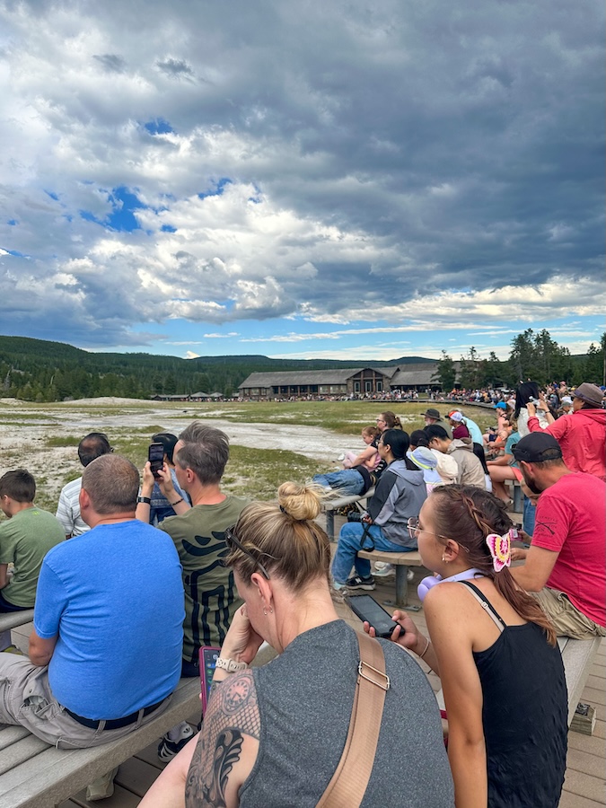 Visitors sitting on benches around Old Faithful waiting for the geyser to erupt in Yellowstone National Park.