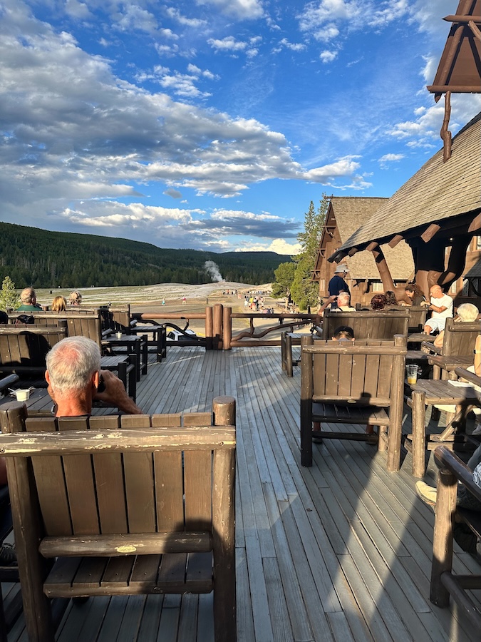 Outdoor deck at Old Faithful Inn with wooden chairs and a view of Old Faithful in Yellowstone National Park.