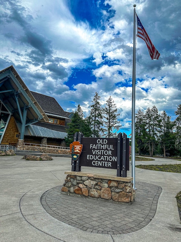 Old Faithful Visitor Education Center entrance sign and American flag in Yellowstone National Park.