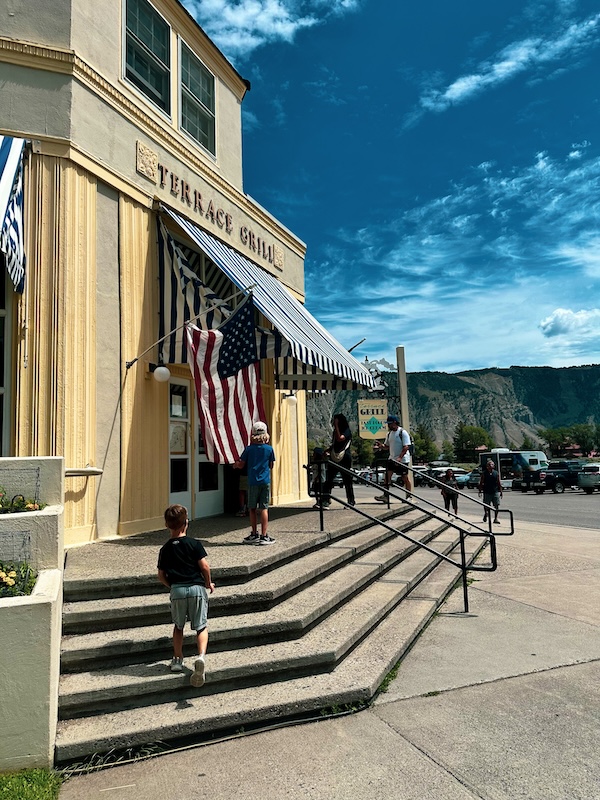 Exterior of Terrace Grill at Mammoth Hot Springs in Yellowstone National Park with families walking toward the entrance.