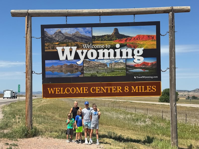 Family standing beneath the Welcome to Wyoming sign along the highway near the Northeast Wyoming Welcome Center.