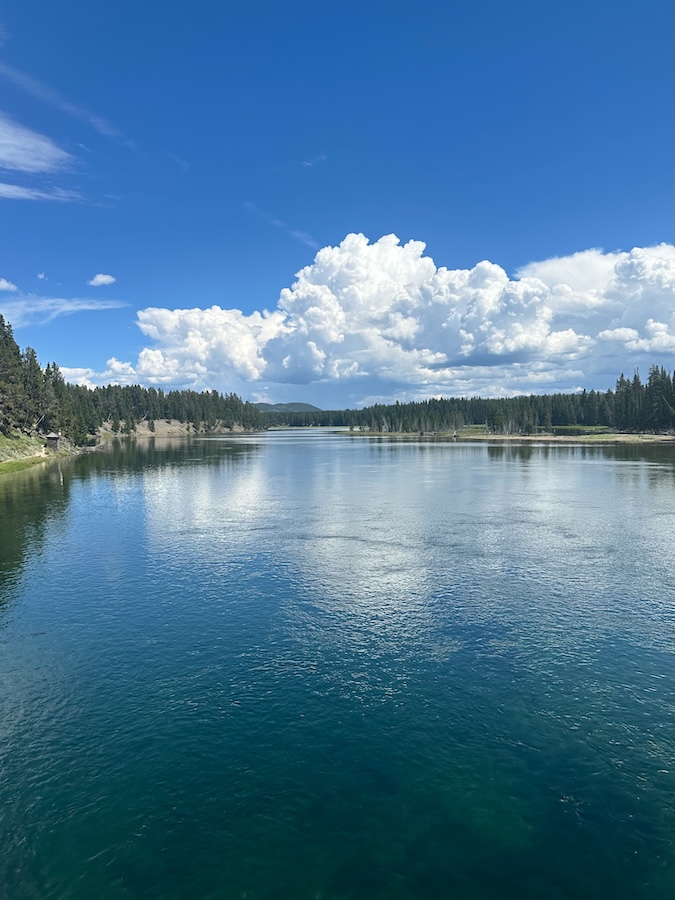 Calm Yellowstone River reflecting blue skies and clouds as seen from Fishing Bridge in Yellowstone National Park.