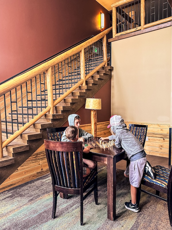 Children playing chess at a table in a common area inside Rhyolite Lodge at Canyon Lodge in Yellowstone